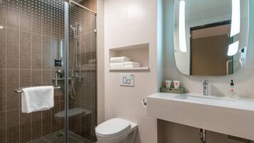 Un baño moderno con cabina de ducha de vidrio, inodoro, lavabo con espejo y un perchero para toallas.