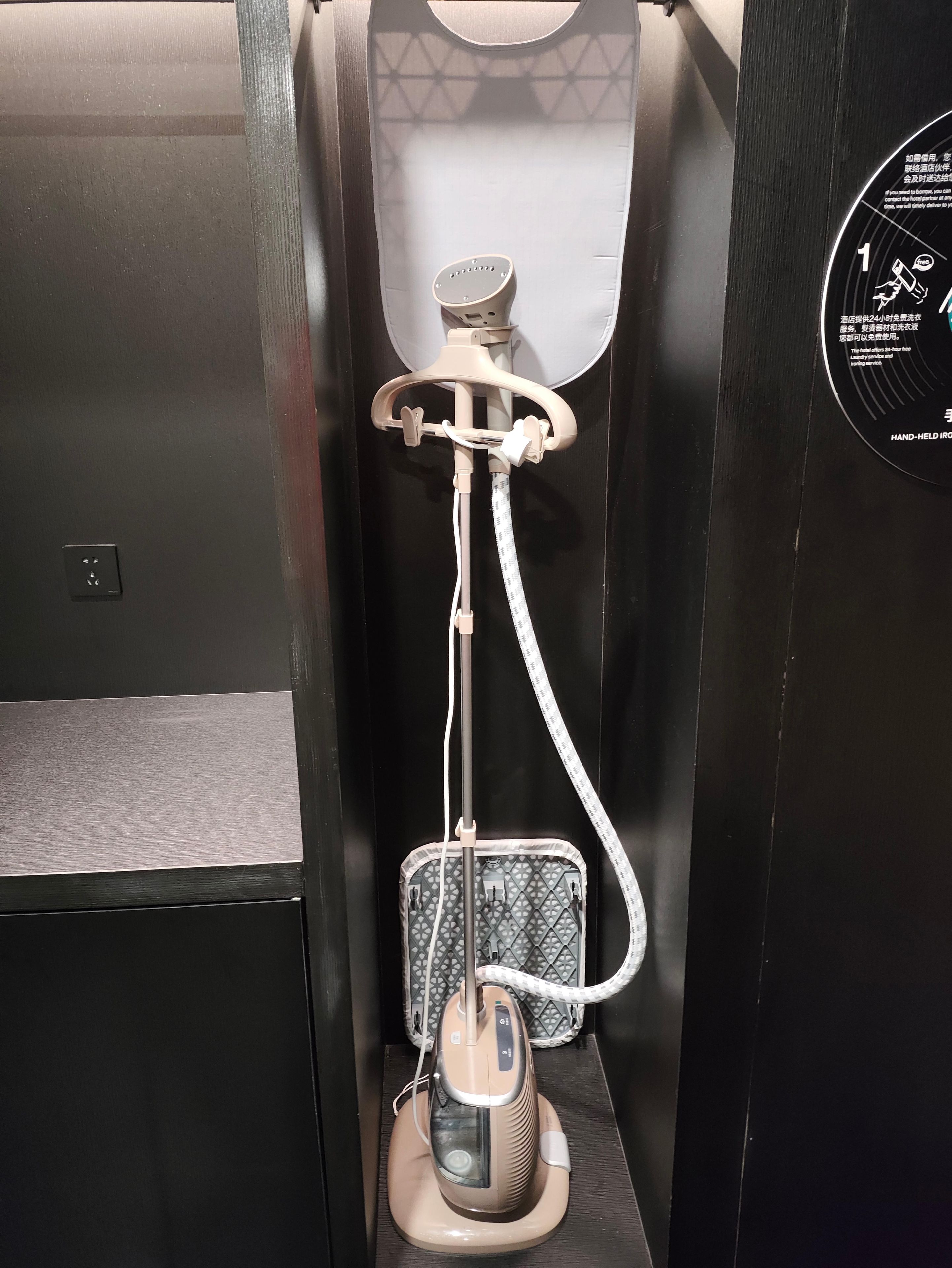 A hand-held hairdryer in a bathroom stall with a towel hanging on the wall and a sign with instructions.