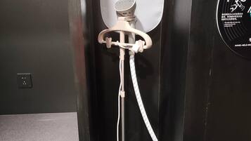 A hand-held hairdryer in a bathroom stall with a towel hanging on the wall and a sign with instructions.