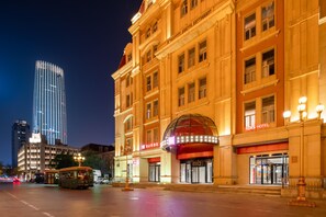 Um hotel com uma entrada em cúpula destacada, um toldo vermelho e uma placa com a inscrição 'IBIS HOTEL'.