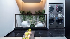 A modern laundry room with two stacked washing machines, a glass display case with decorative items, and a black tiled floor. - Ibis Hotel Tianjin Railway Station Jinwan Plaza (Tianjin)