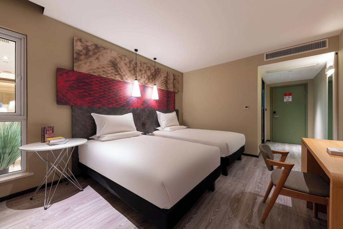 Ein Hotelzimmer mit zwei Betten, einem kleinen Tisch, einem Stuhl und einem großen, abstrakten Gemälde an der Wand.
