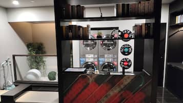 Un baño moderno con ducha, lavamanos y espejo. Hay estanterías con libros y objetos decorativos.