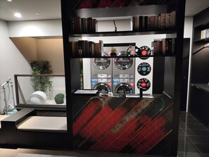 Un baño moderno con ducha, lavamanos y espejo. Hay estanterías con libros y objetos decorativos.
