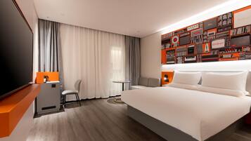A modern hotel room with a large bed, a desk with a chair, a small table, and a wall with vintage radio and television designs.
