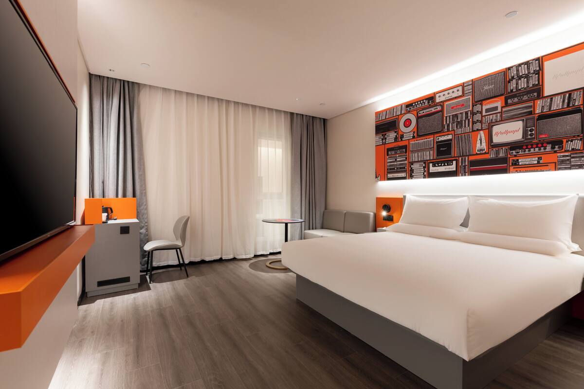 Ein modernes Hotelzimmer mit einem großen Bett, einem Schreibtisch, einem Sessel, einem kleinen Tisch und einer Wand, die mit Vintage-Radiogeräten dekoriert ist.