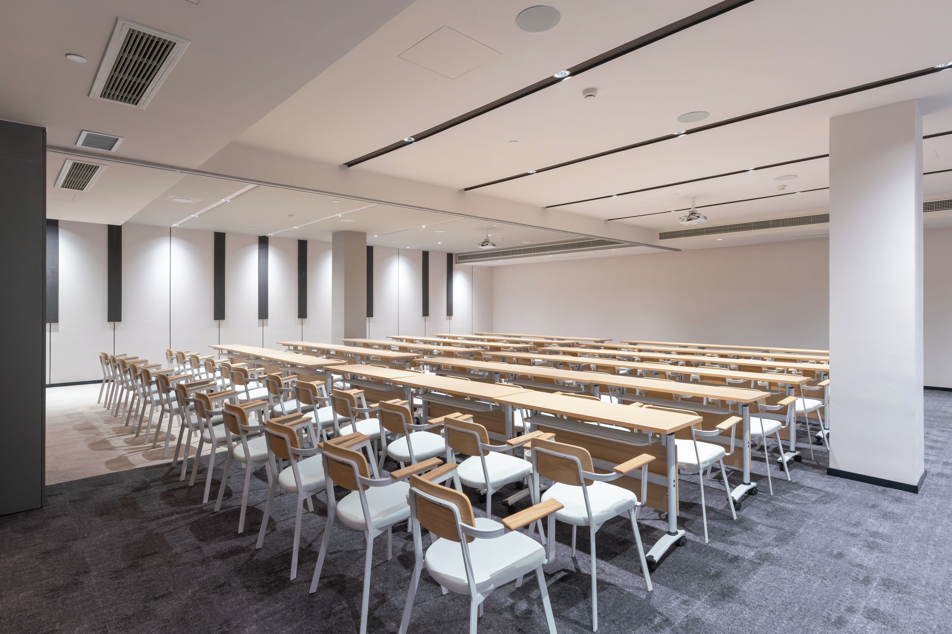 Ein Konferenzraum mit Tischen und Stühlen, einem Teppichboden und einer weißen Decke mit Lüftungsanlage.