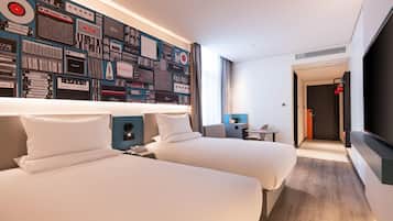 A hotel room with two beds, a wall of vintage audio equipment, a TV, and a door leading to another room.