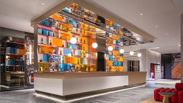 A modern hotel lobby with a central reception desk, a seating area with red sofas, and a decorative wall with various items. - Ibis Hotel Tianjin Railway Station Jinwan Plaza (Tianjin)