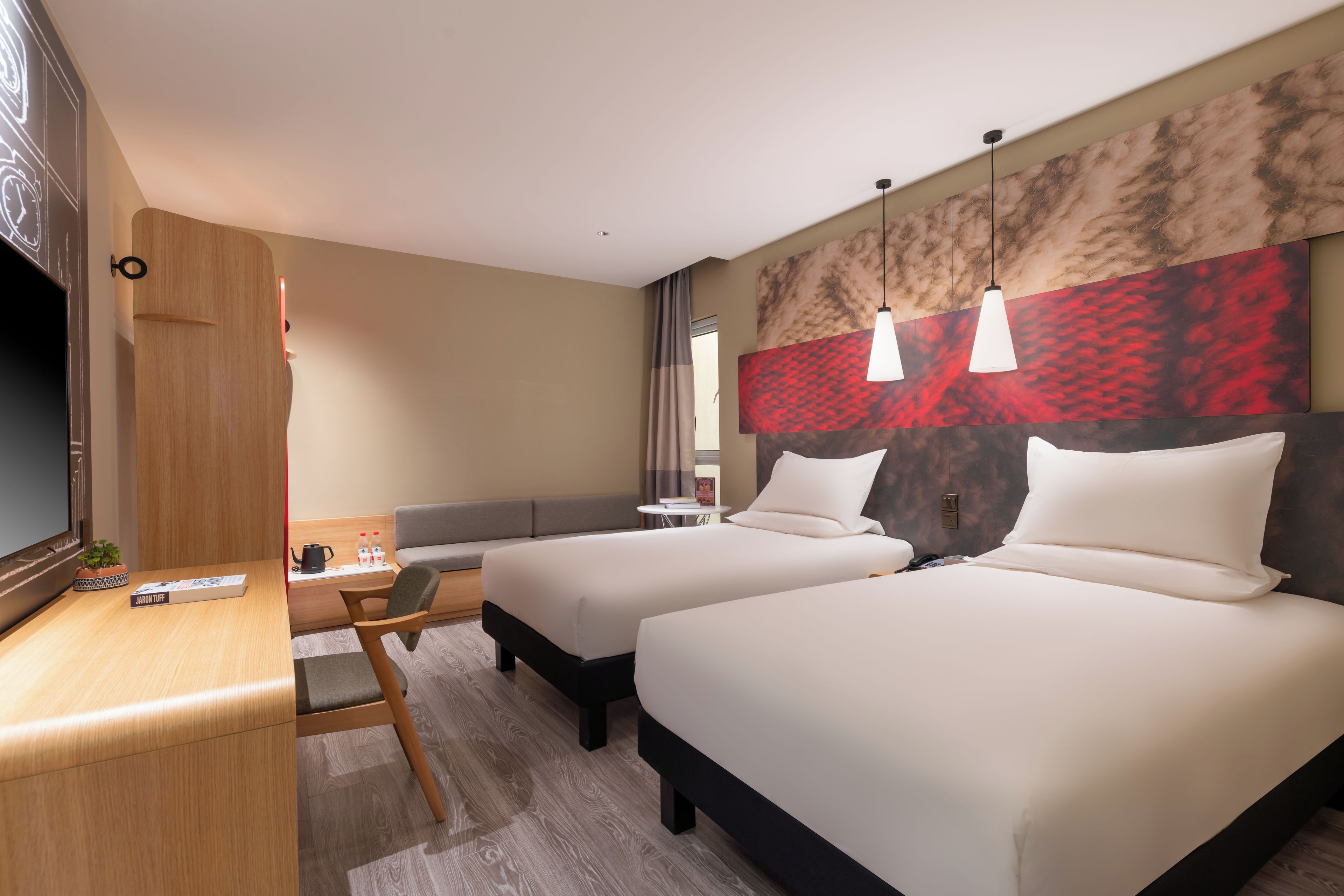 A hotel room with two beds, a desk, a chair, a TV, and a large abstract painting on the wall.