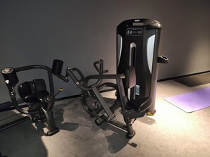 Une salle de sport équipée de matériel d’exercice, notamment une machine pour les exercices de développé couché et une machine pour les exercices de presse à cuisses.