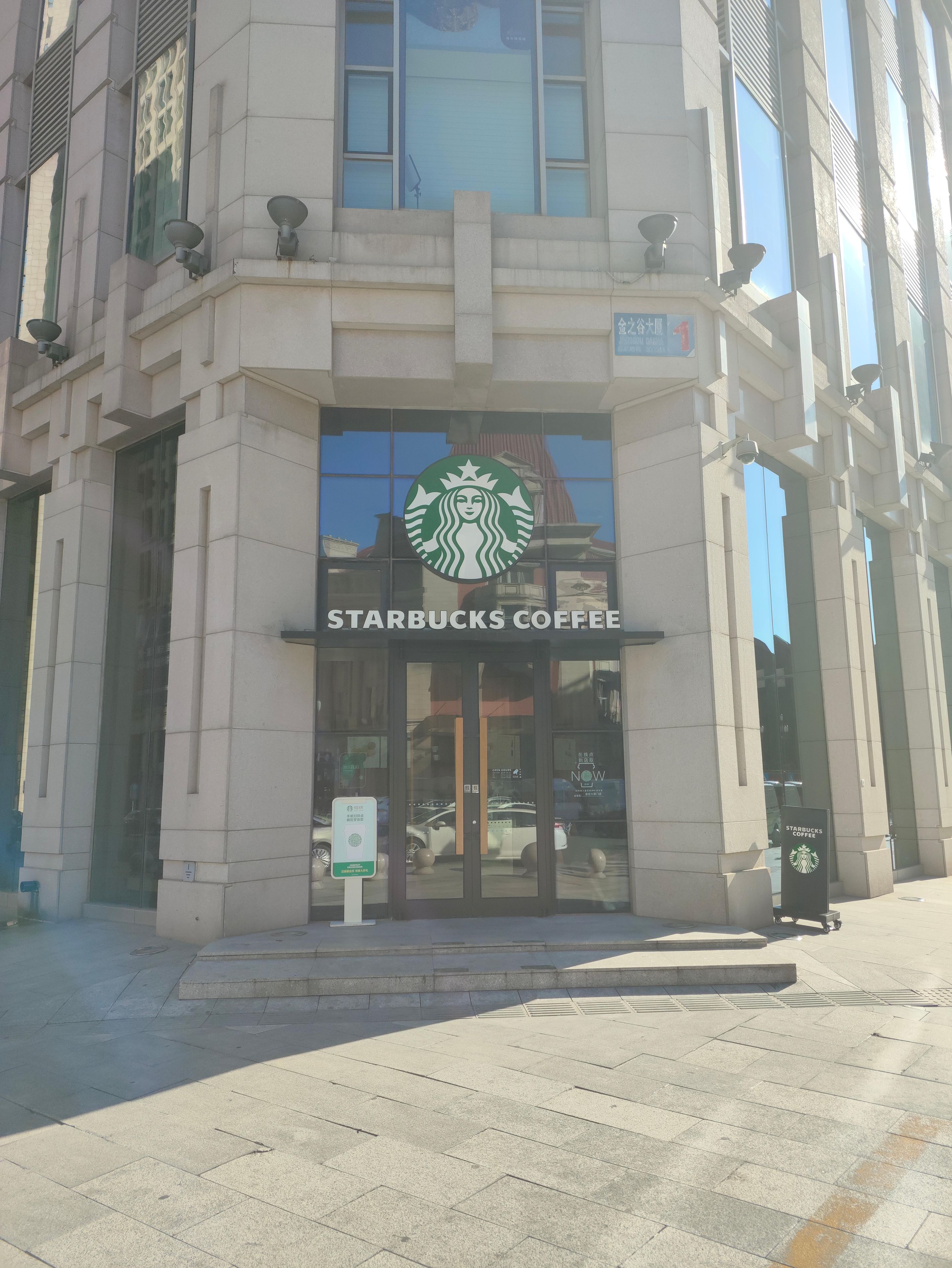 A Starbucks Coffee storefront with a glass entrance, a signboard, and a parking sign.