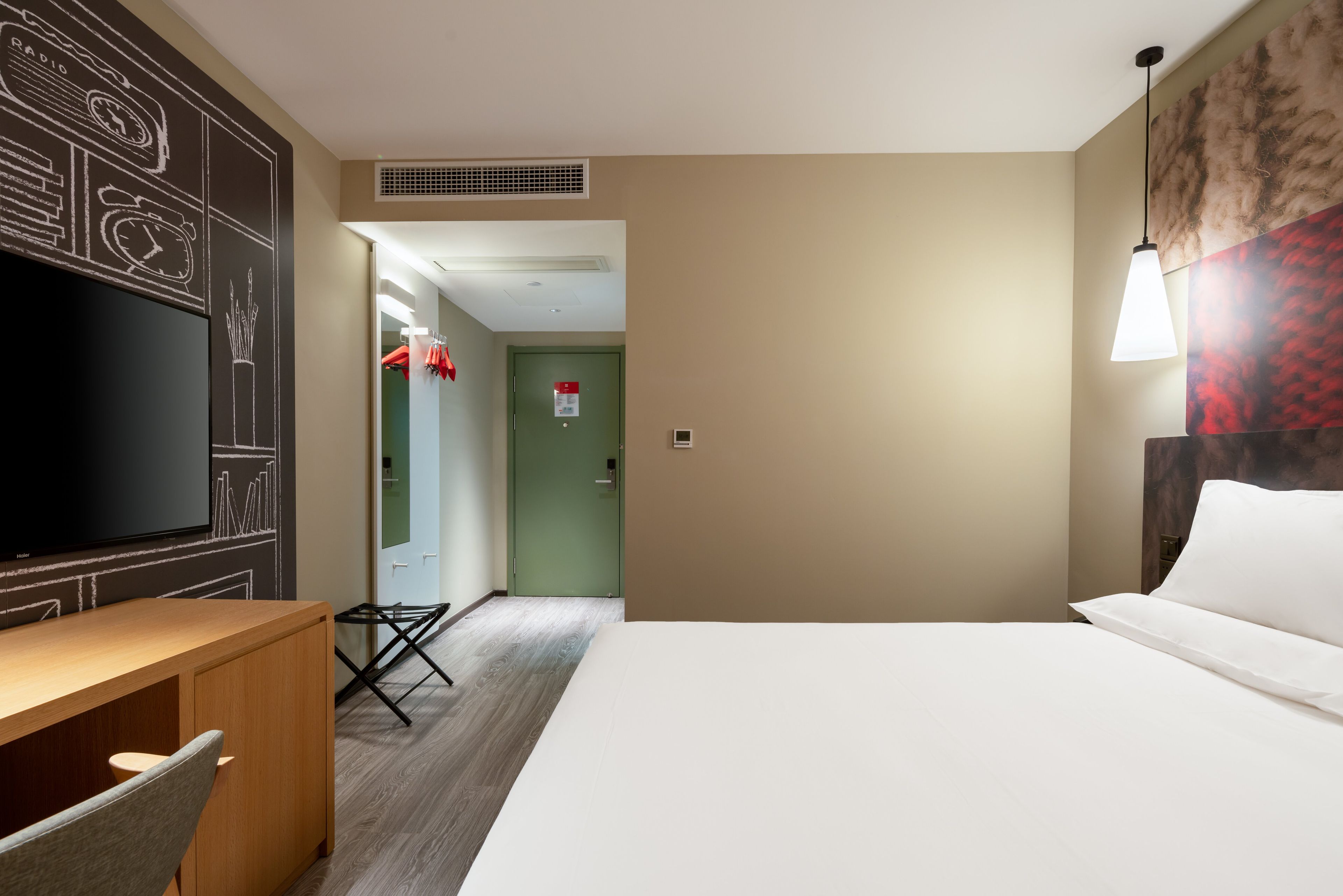 A hotel room with a bed, a desk with a chair, a flat-screen TV, and a wall with a chalkboard design.