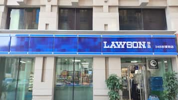 Un magasin LAWSON avec une enseigne bleue, une vitrine en verre et une plante en pot à l’extérieur.