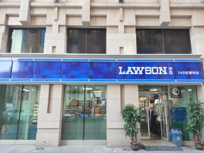 Un magasin LAWSON avec une enseigne bleue, une vitrine en verre et une plante en pot à l’extérieur.