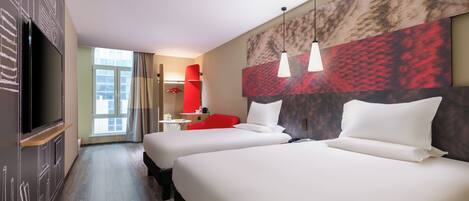 A hotel room with two beds, a TV, a red chair, and a large window.
