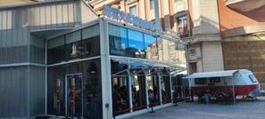 Un edificio moderno con facciata in vetro, un cartello sopra l'ingresso e un autobus parcheggiato davanti.