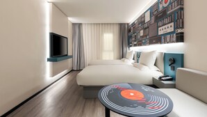 A modern hotel room with a bed, a flat-screen TV, a round table with a vinyl record design, a sofa, and a wall with vintage audio equipment. - Ibis Hotel Tianjin Railway Station Jinwan Plaza (Tianjin)