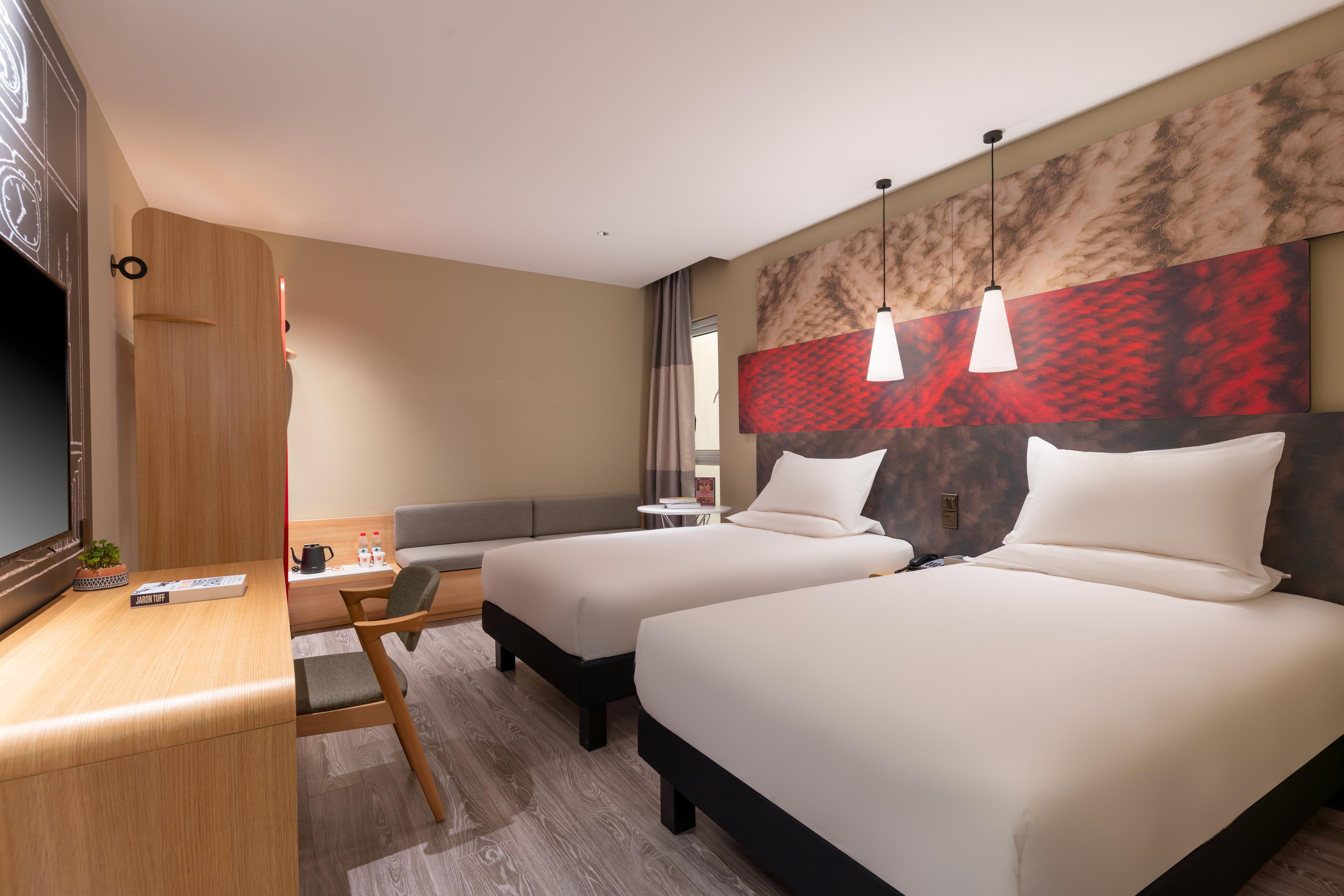 A hotel room with two beds, a desk, a chair, a TV, and a large abstract wall painting.
