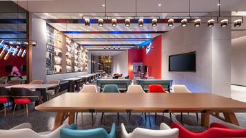 Un restaurante moderno con una larga mesa de madera, sillas coloridas y una zona de bar con estanterías.