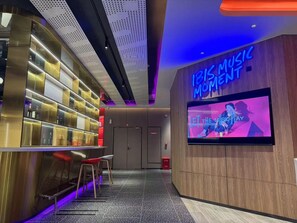 A modern bar area with a neon sign reading 'Let the Music Play,' a TV screen, and a bar counter with stools. - Ibis Qingdao Xinduxin Capitamall Hotel (Qingdao)
