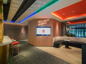 Un intérieur moderne comprenant un espace salon, un écran numérique affichant le logo d’Ibis et un mur d’accent en bois.