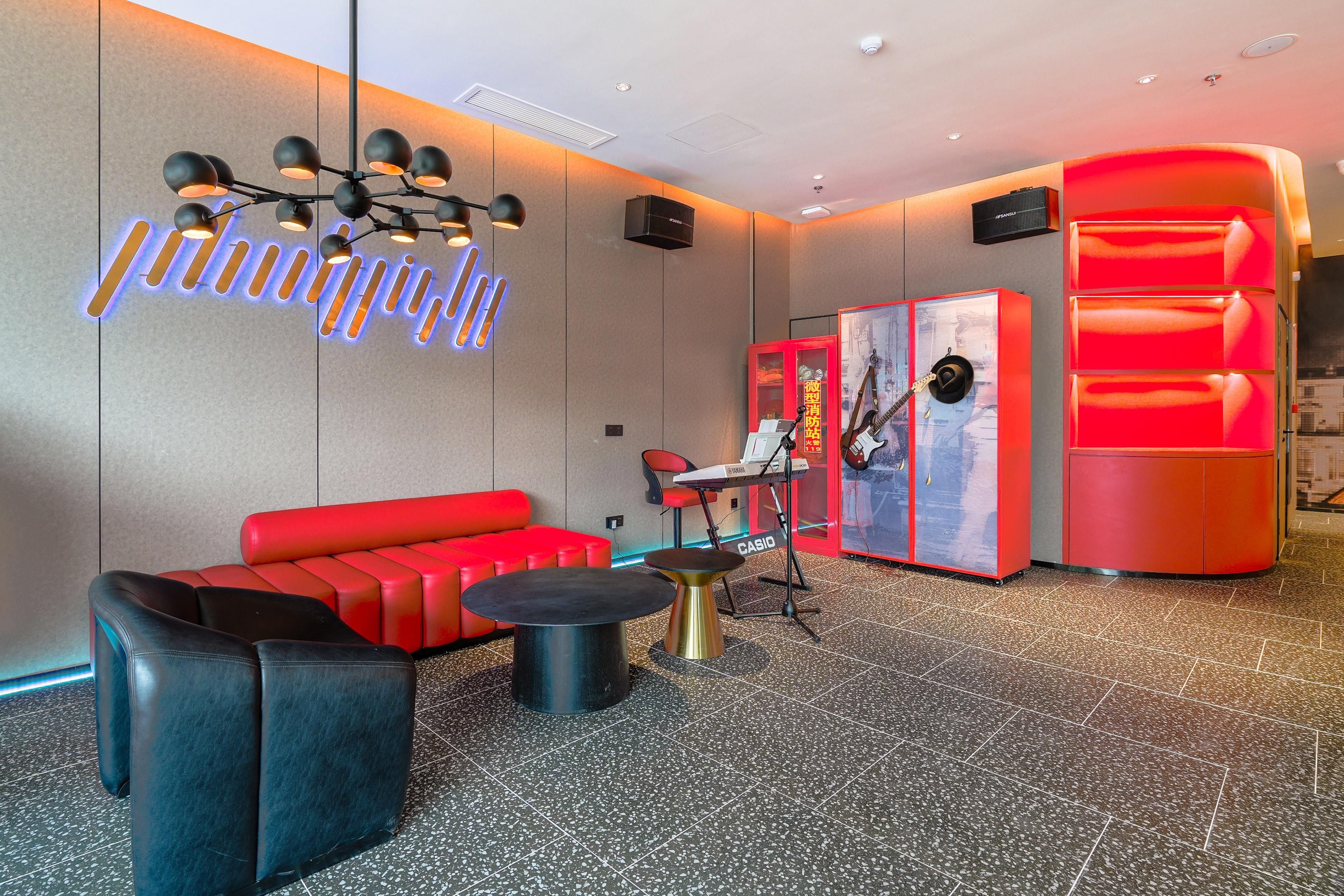A modern lobby with a red sofa, black chairs, a black coffee table, a neon sign, a red cabinet, and a keyboard.