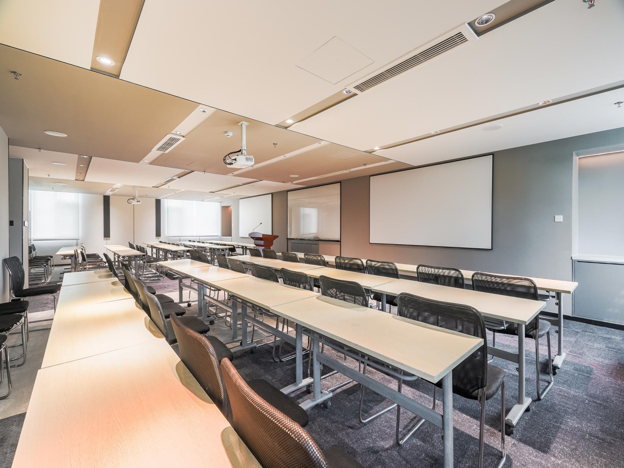 A conference room with long tables, chairs, a projector, and a screen.