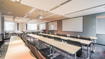 A conference room with long tables, chairs, a projector, and a screen.