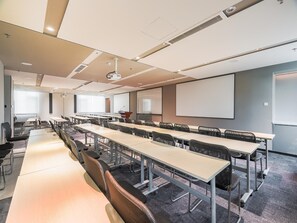 A conference room with long tables, chairs, a projector, and a screen. - Ibis Qingdao Xinduxin Capitamall Hotel (Qingdao)