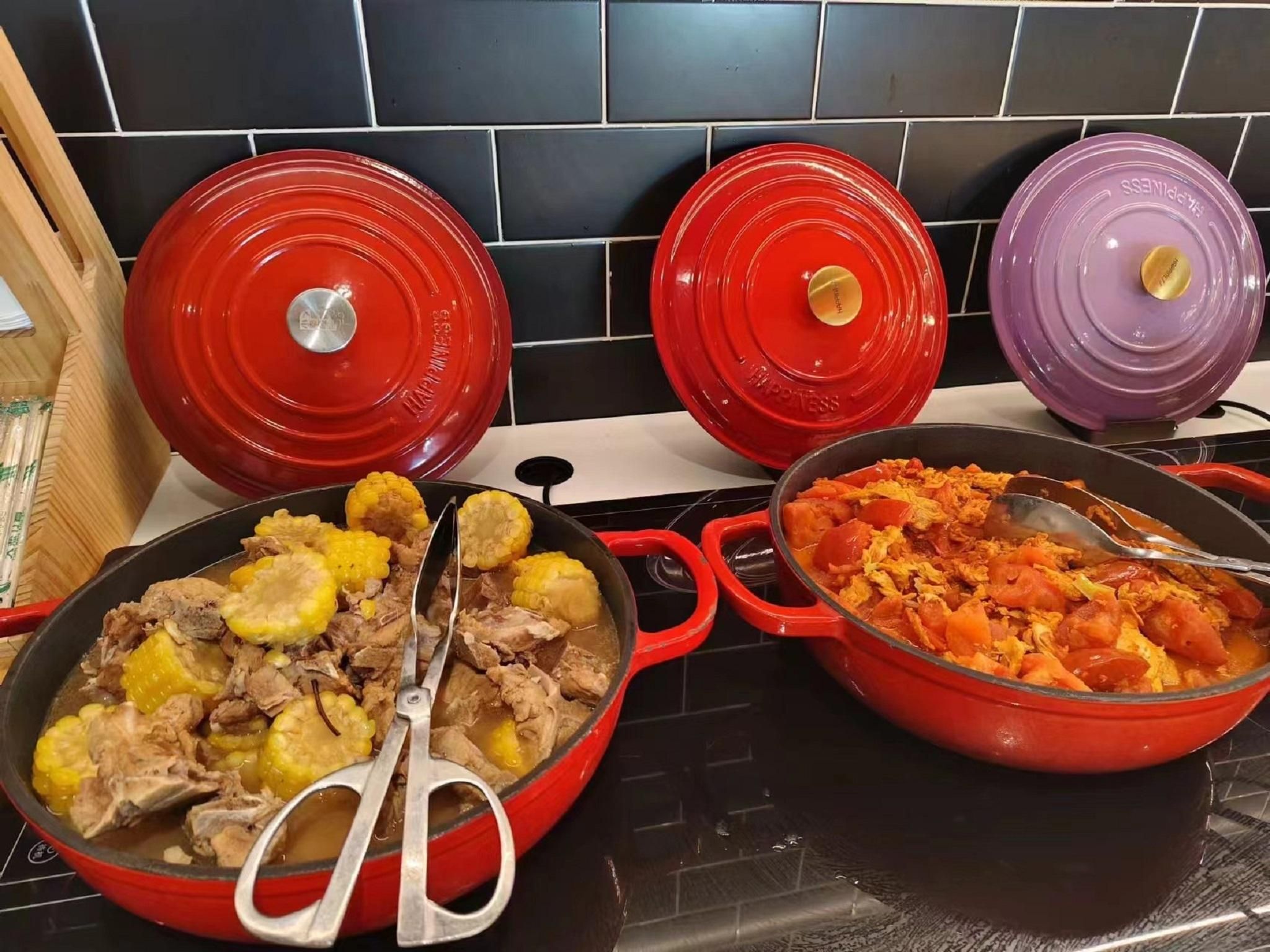 A kitchen with two red pots on a stove, one with a lid and the other open, revealing food inside.