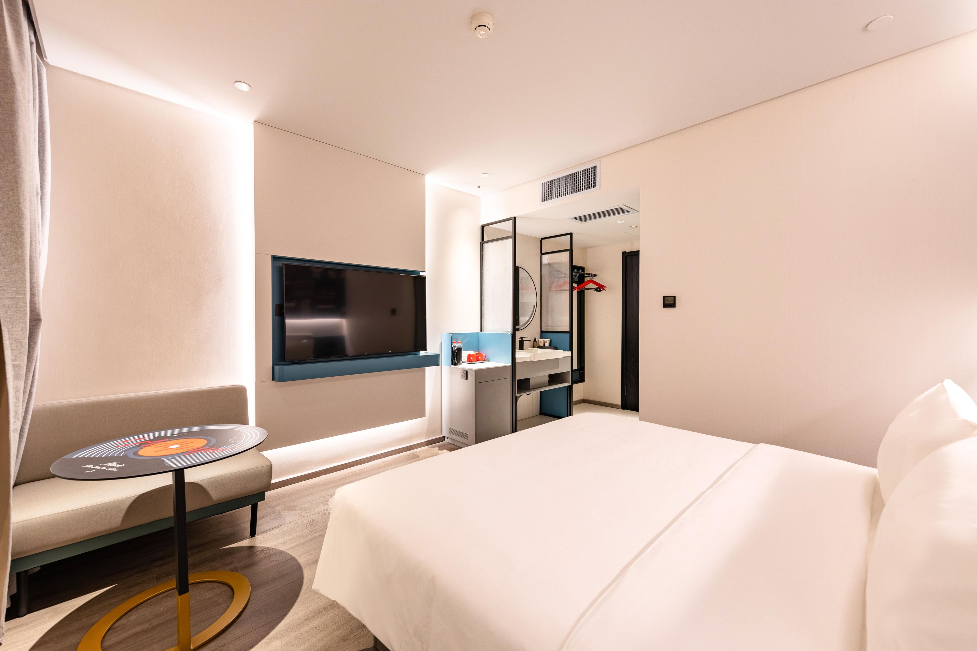 Une chambre d’hôtel comprenant un lit, une télévision, une petite table, un canapé et une salle de bain avec un miroir et un lavabo.