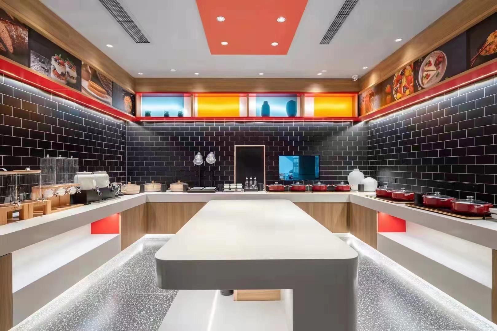A modern kitchen with a central island, black tiled walls, and red accents.