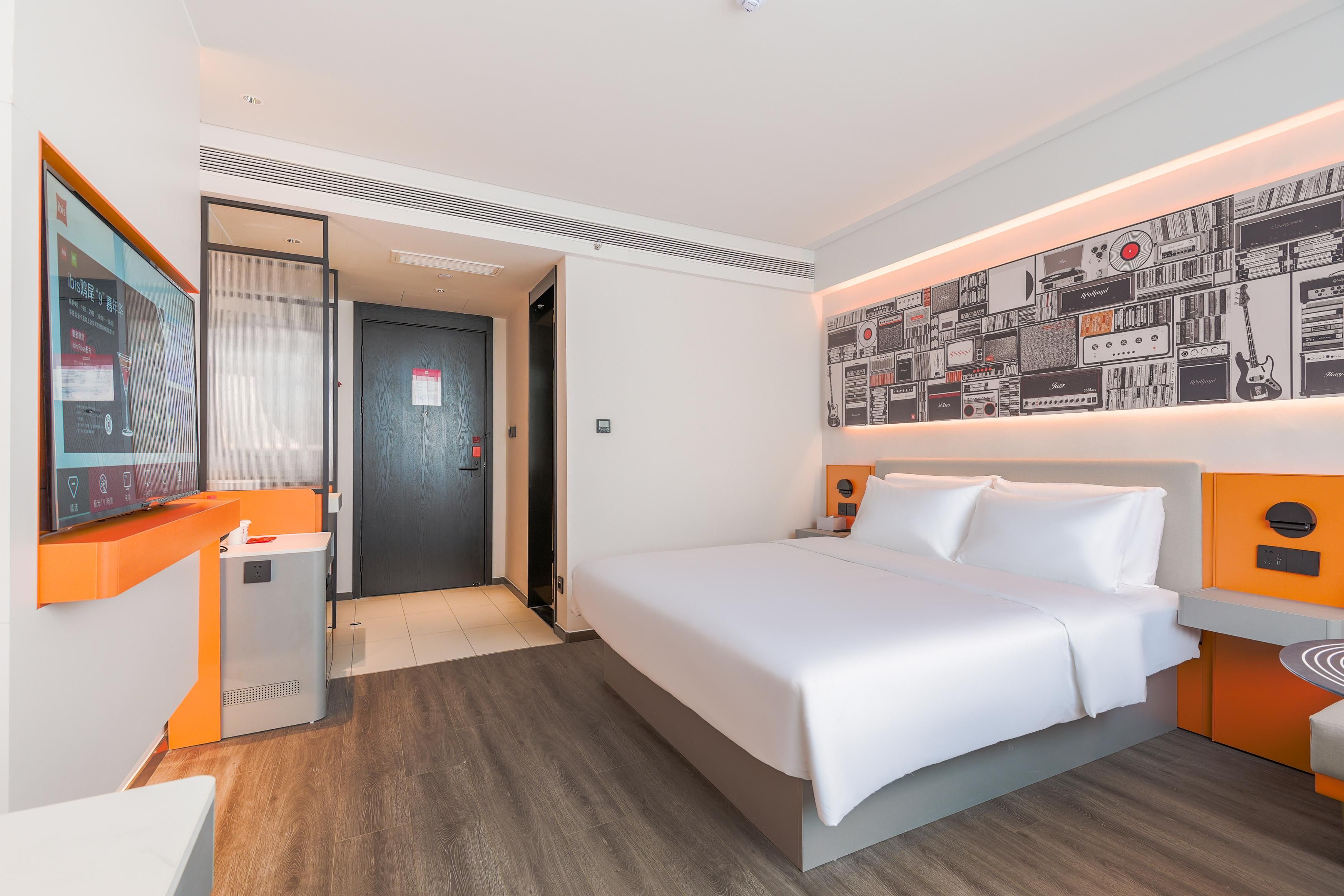 A hotel room with a bed, a desk, a wall-mounted artwork, and a door.