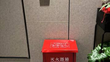 Een brandblusserbehuizing met de tekst 'FIRE ALARM 119' en een rookmelder aan de muur.