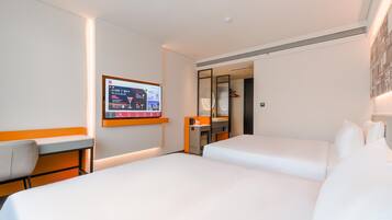 Een hotelkamer met een bed, een bureau, een stoel, een aan de muur bevestigde televisie en een spiegel.