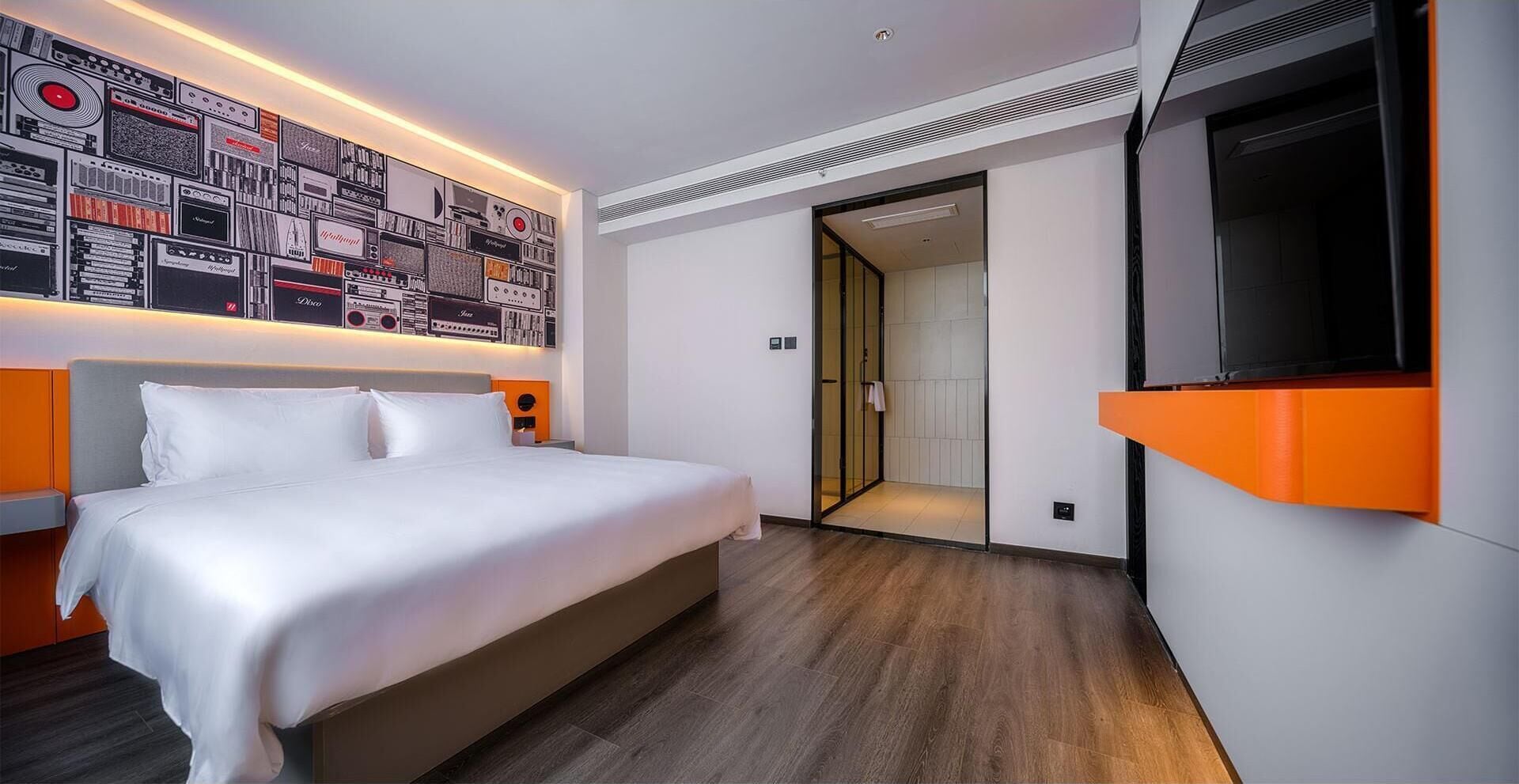 A modern hotel room with a large bed, a wall-mounted TV, and a unique wall art display.