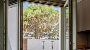 Eine geöffnete Schiebetür führt auf eine Außenpatio mit Tisch und Stühlen, mit Blick auf Bäume, sowie eine Küchenzeile mit Schränken und einer Arbeitsplatte.