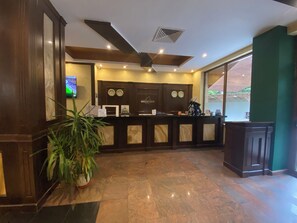 A reception area with a marble floor, wooden reception desk, wall-mounted clocks, and a television screen. - Hotel Iceberg (Sofia)
