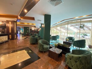 A lobby with a reception desk, seating area, and a glass-enclosed pool. - Hotel Iceberg (Sofia)