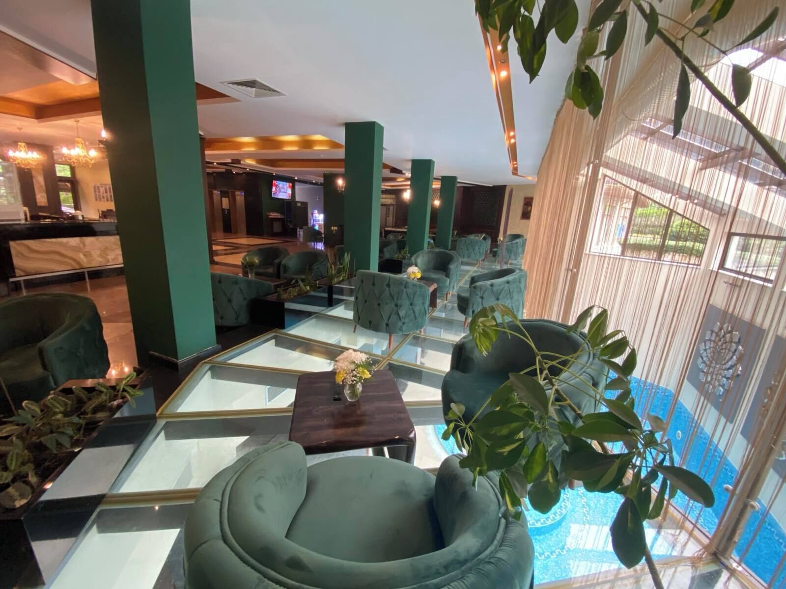 A lobby with a pool, green upholstered chairs, and a glass coffee table.