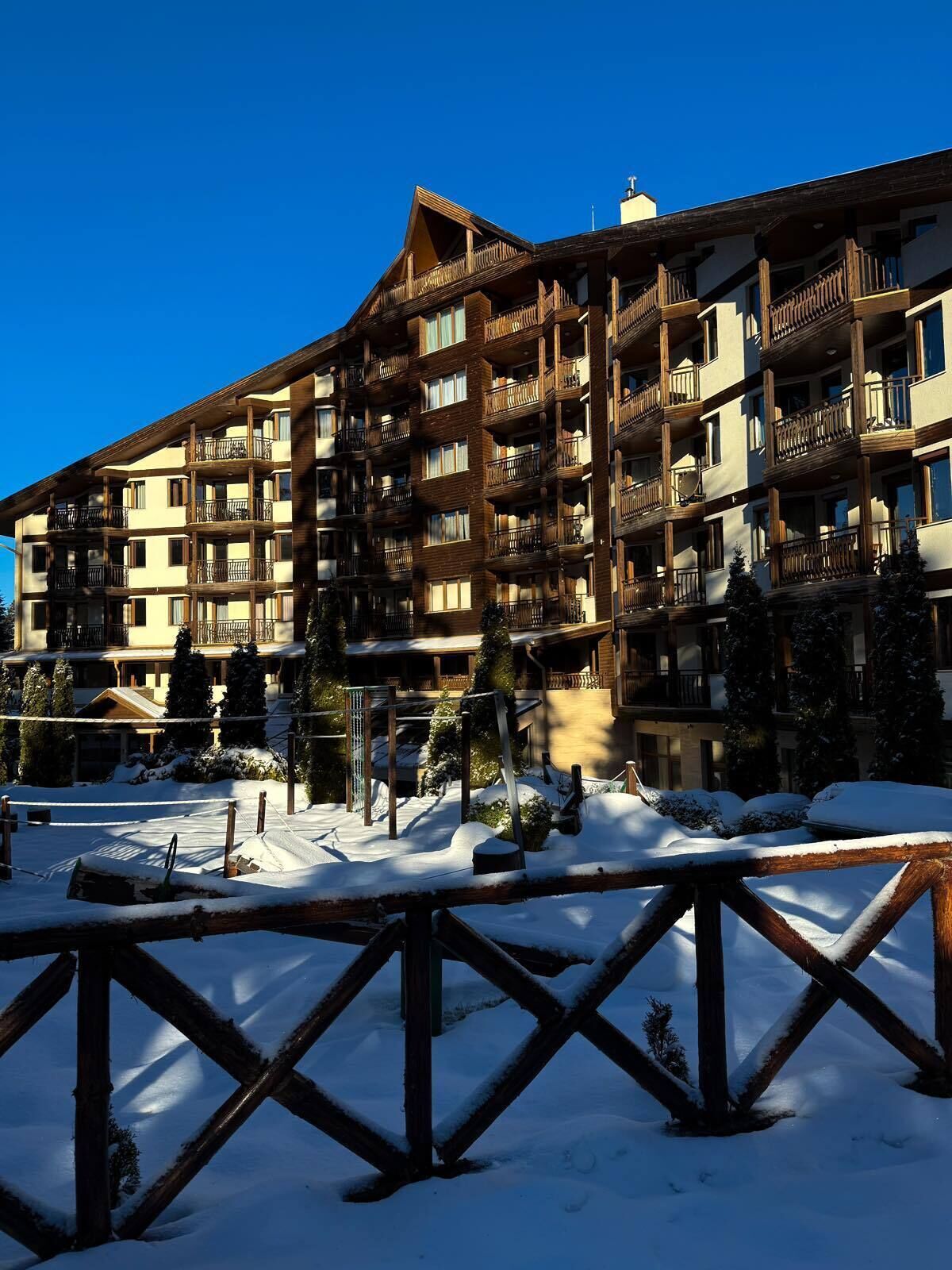 A multi-story hotel with balconies, a ski slope in the foreground, and snow-covered surroundings.