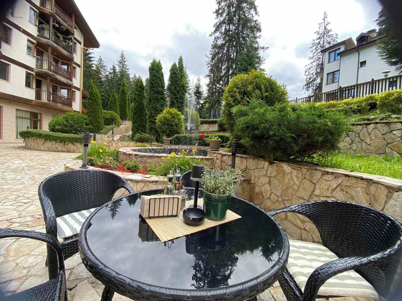 A courtyard with a round glass table, wicker chairs, a stone wall, and a building with balconies.