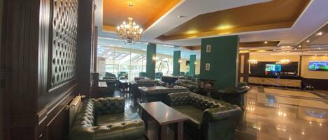 A lobby with leather sofas, a chandelier, a reception desk, and a large screen.
