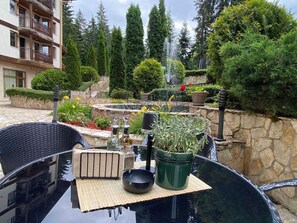 A patio area with a table, chairs, a potted plant, a fountain, and a stone wall. - Hotel Iceberg (Sofia)