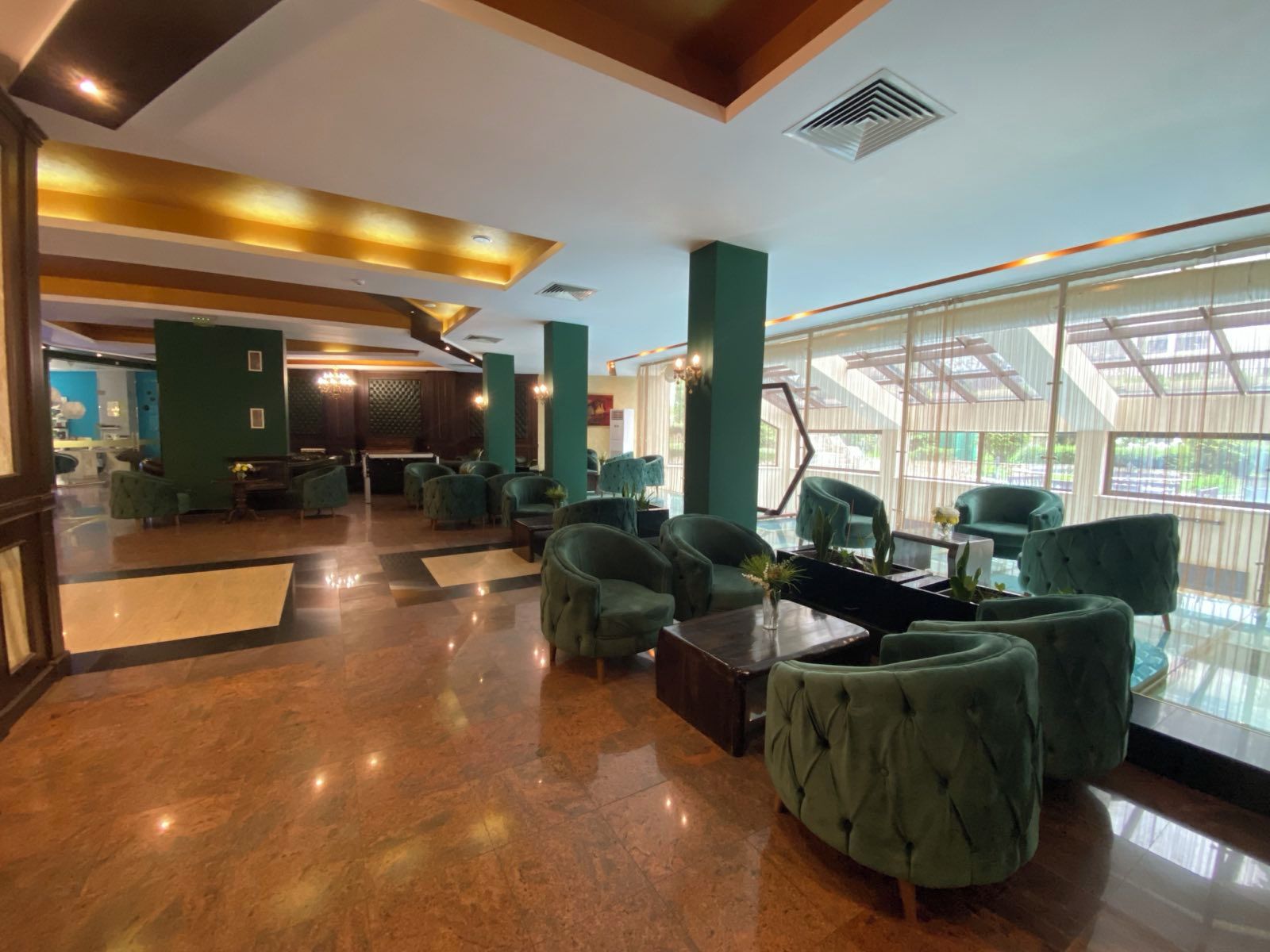 Un vestíbulo con sillones tapizados en verde, piso de mármol y ventanas amplias.