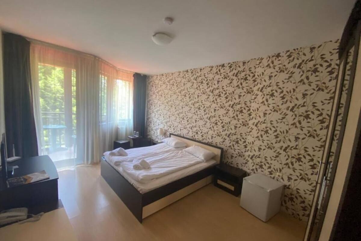 A modern hotel room with a large bed, a desk, and a view of the outdoors.