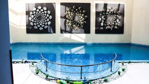 An indoor swimming pool with a tiled edge, surrounded by a metal railing, and three abstract wall art pieces above. - Hotel Iceberg (Sofia)