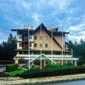 A multi-story hotel with a restaurant on the ground floor, surrounded by greenery and a clear sky. - Hotel Iceberg (Sofia)