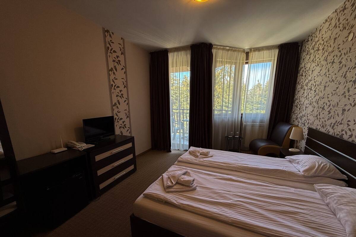 A hotel room with a bed, a desk with a television, a chair, and a window with curtains.